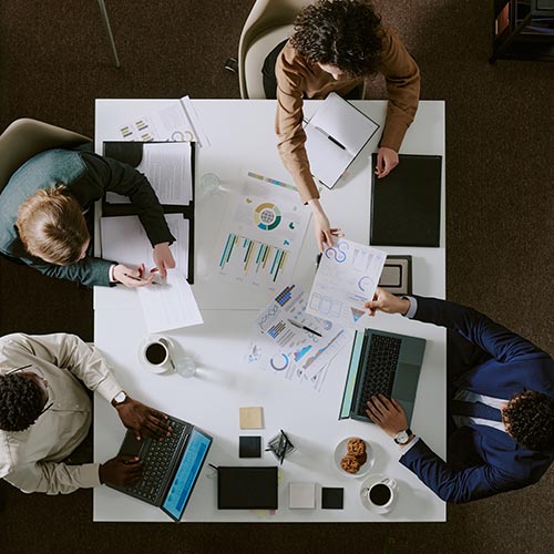 overview of four people sitting at a square table working on laptops and papers