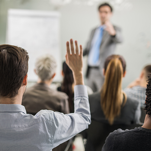 man raising his hand in a classroom and teachers face is out of focus