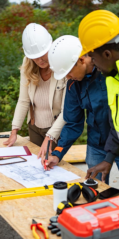 one woman and two men in hard hats looking over construction plans
