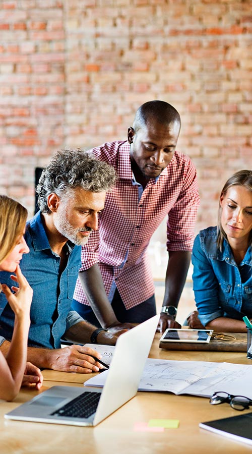 4 people sitting at a table going over papers with laptops and sitting in front of a brick wall