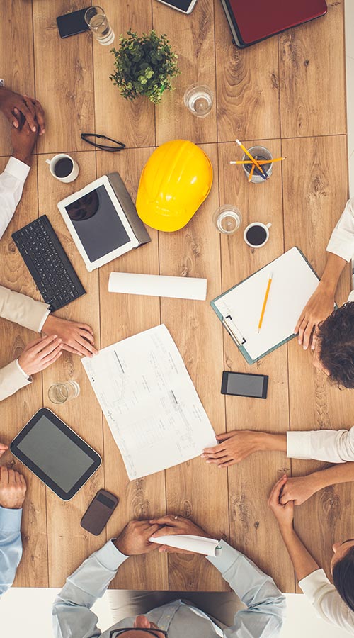 overview of people sitting at large table with laptops, papers and a hard hat