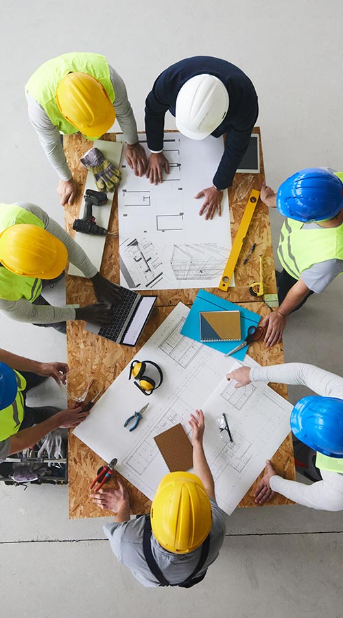 overhead view of a group on construction workers and code officials looks over plans on a makeshift table