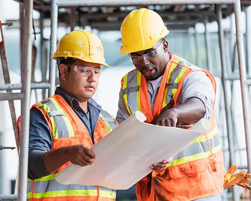 two men on a construction site looking at blue prints together